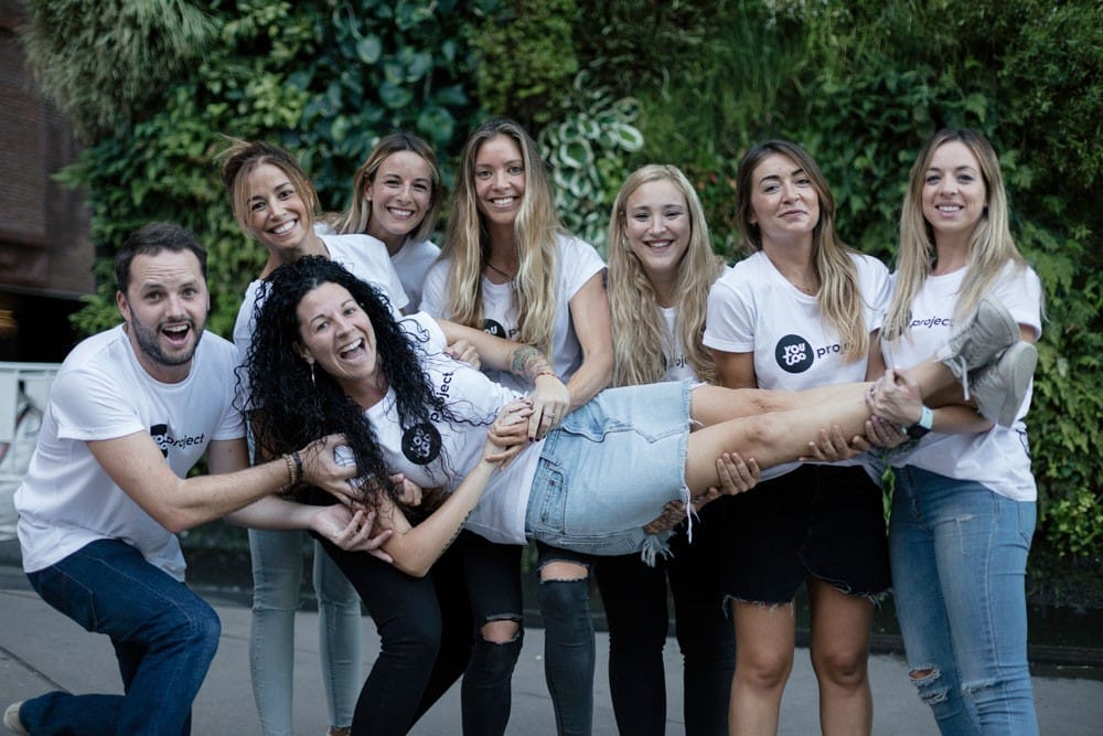 Hacer ejercicio grupo de la empresa AUssieYouTOO en un evento en madrid. Todos llevan la camiseta de YouTOOProject de color blanca. Están sonriendo y sujetando a Marta Caparrós